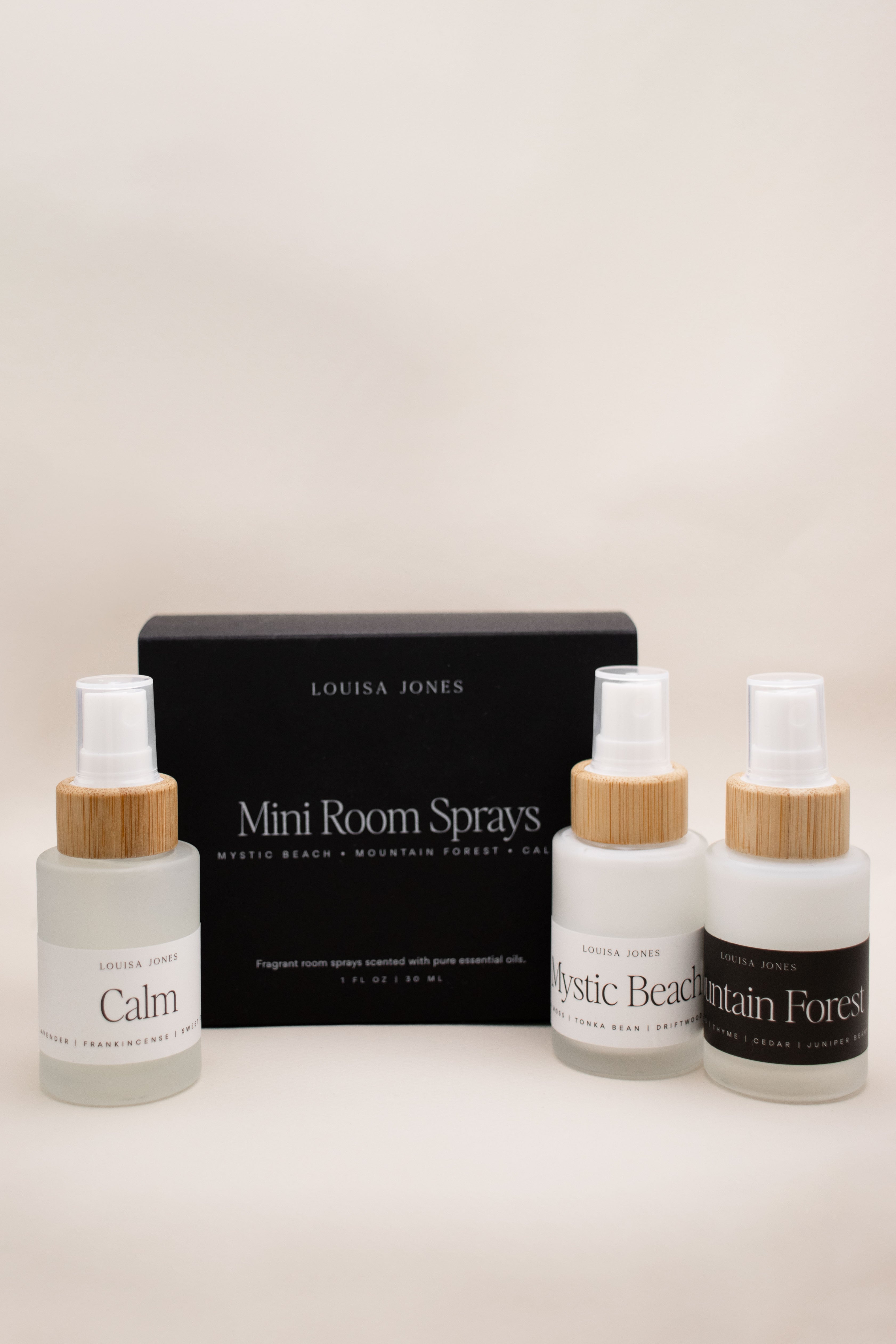 Three mini room spray bottles with bamboo caps and black boxes on a beige background